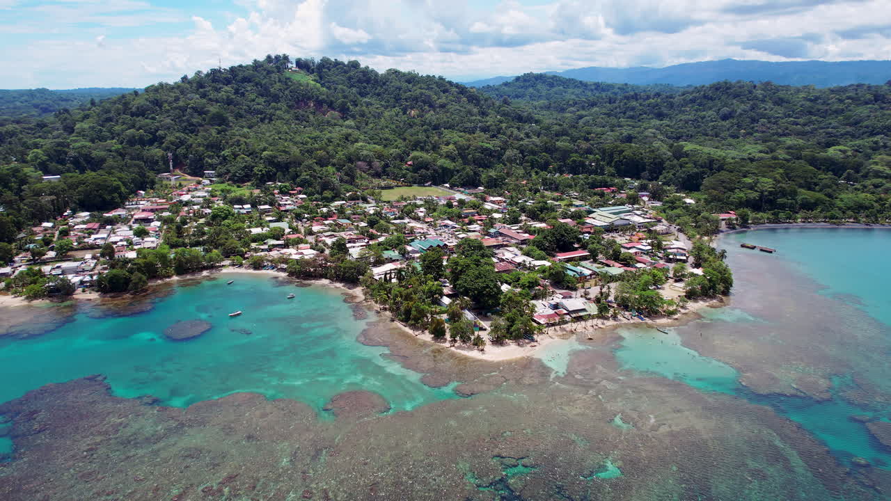 Wide aerial of downtown Puerto Viejo, a popular tourism destination on the Caribbean coast of Costa Rica, with a lush, tropical landscape of jungle mountains and scenic turquoise clear water beaches.