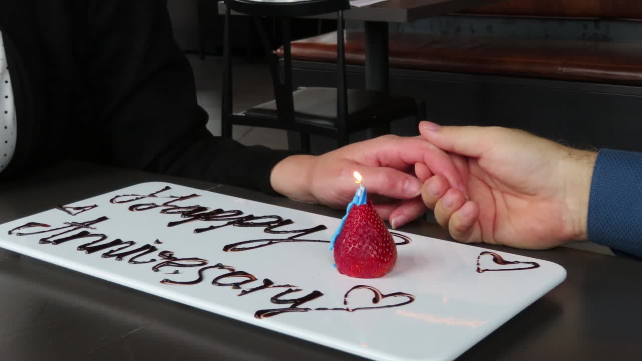 장식 쓰기와 촛불 축 하와 함께 레스토랑에서 손을 잡고 행복 한 기념일 커플