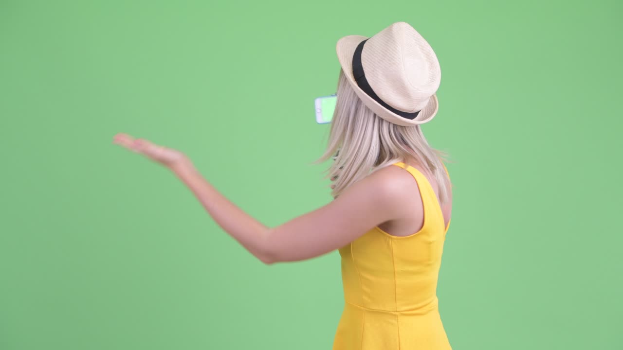 젊은 관광객 여성 인플루언서가 휴대전화를 사용하여 녹색 배경에 대해 블로그를 하는 스튜디오 촬영