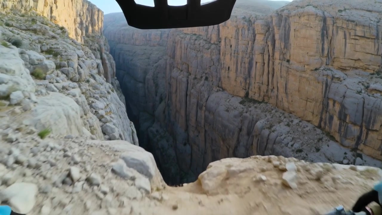 Un ciclista si avvicina a un sentiero stretto, rallenta, sbircia e controlla il dislivello al bordo del canyon, con casco e guanti.