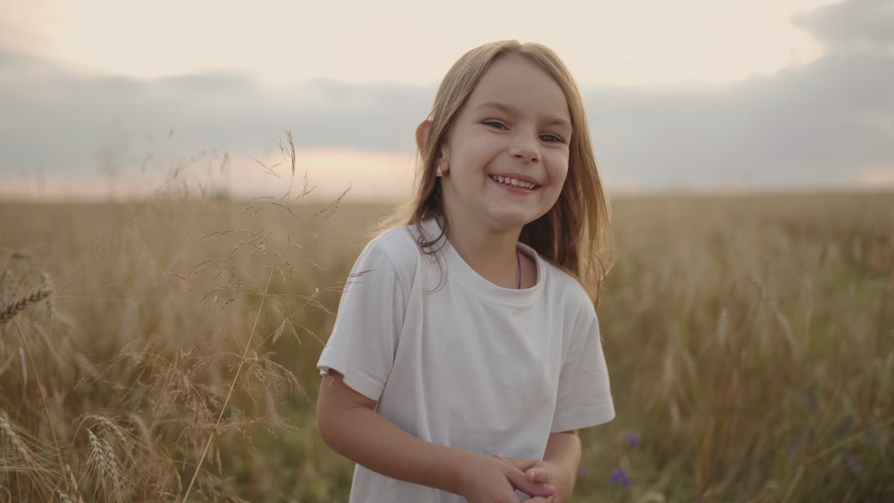 una feliz niña sonriente mirando a la cámara corre en cámara lenta al atardecer en un campo de maíz