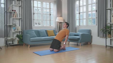 hombre asiático haciendo yoga en postura de camello en la alfombra en casa