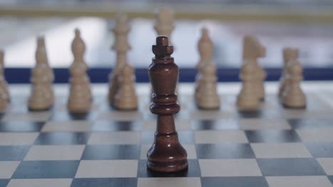 tilt up, black king chess piece faces blurry white army alone, closeup