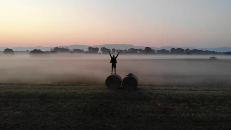 Man-stands-on-round-bale-and-enjoys-the-sunrise