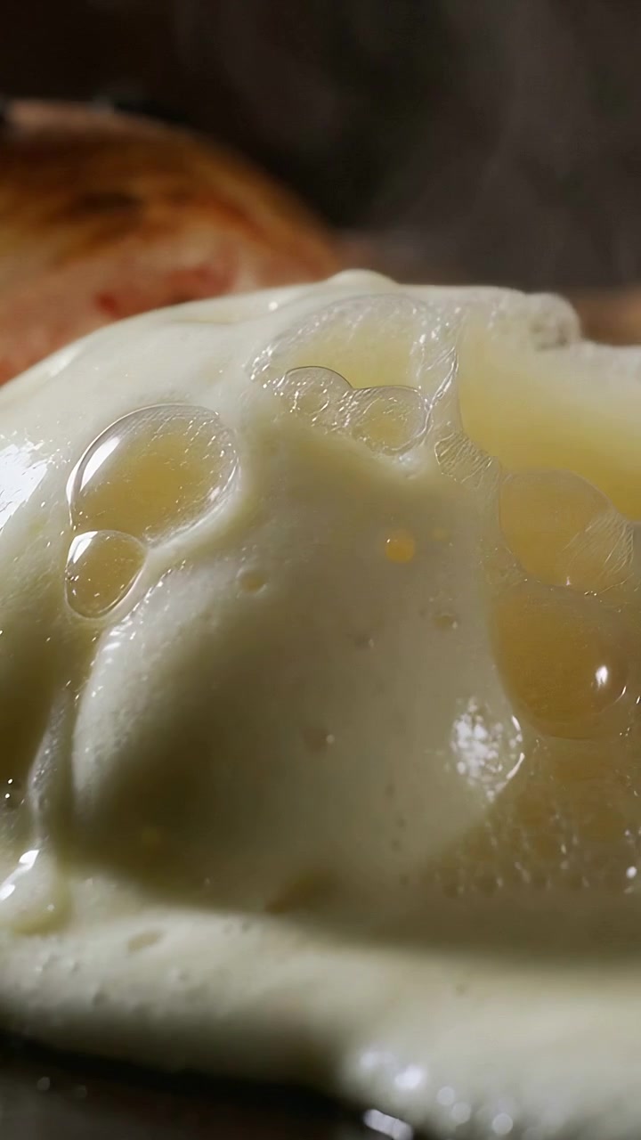 Vertical video: Sizzling fried egg bubbling and spreading from stovetop heat, with bacon and steam