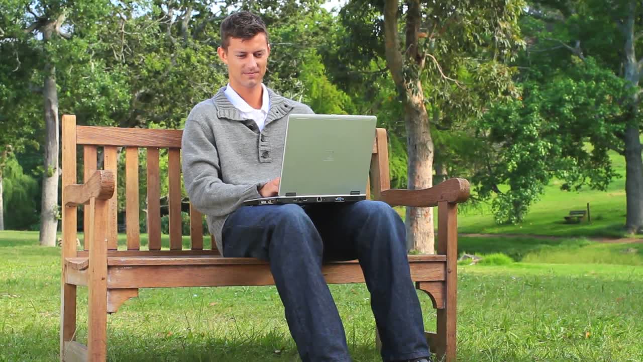 Joven chateando en su portátil en un banco