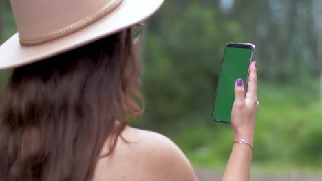 Ein-Mädchen-Mit-Offenem-Haar,-Hut-Und-Brille-Beschäftigt-Sich-Mit-Ihrem-Smartphone-Vor-Einer-Kulisse-Aus-üppigen-Grünen-Bäumen-Und-Gras