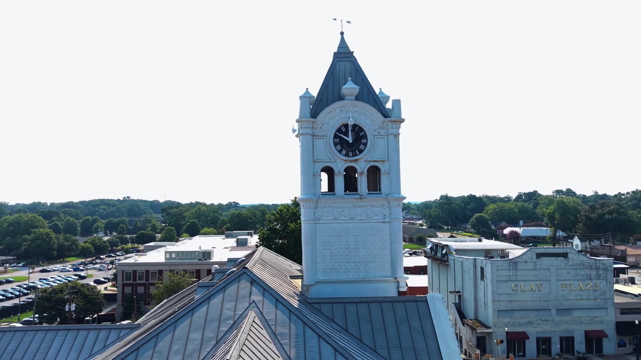 Torre do relógio branca com pináculo eleva-se acima do telhado do tribunal perto de Atlanta, Geórgia, com um estacionamento extenso e edifícios de tijolos espalhados sob uma densa linha de árvores e céu limpo. Vista aérea de drone