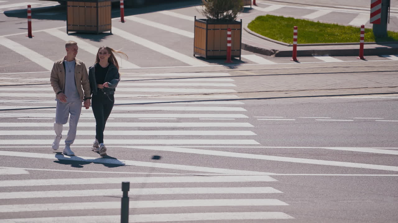 Happy young people walking at the street at the summer. Beautiful girl and blond guy holding hands and walking through the road