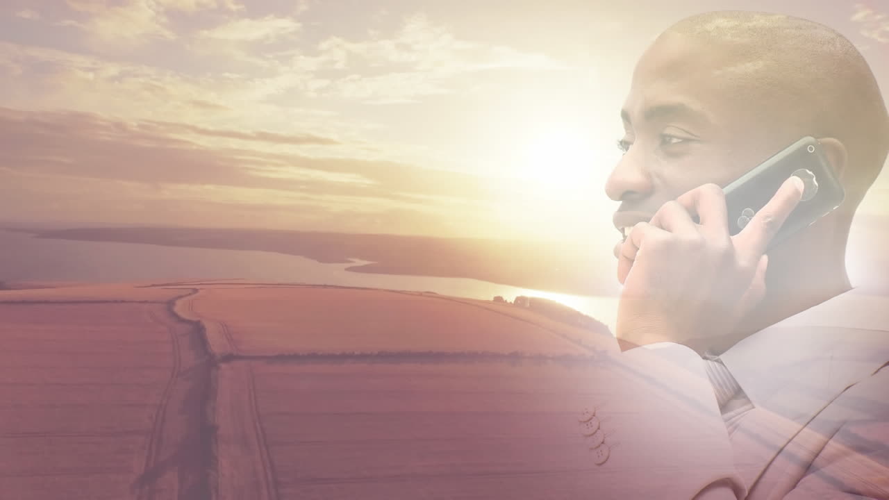 Animation of smiling african american man using smartphone over sunset landscape