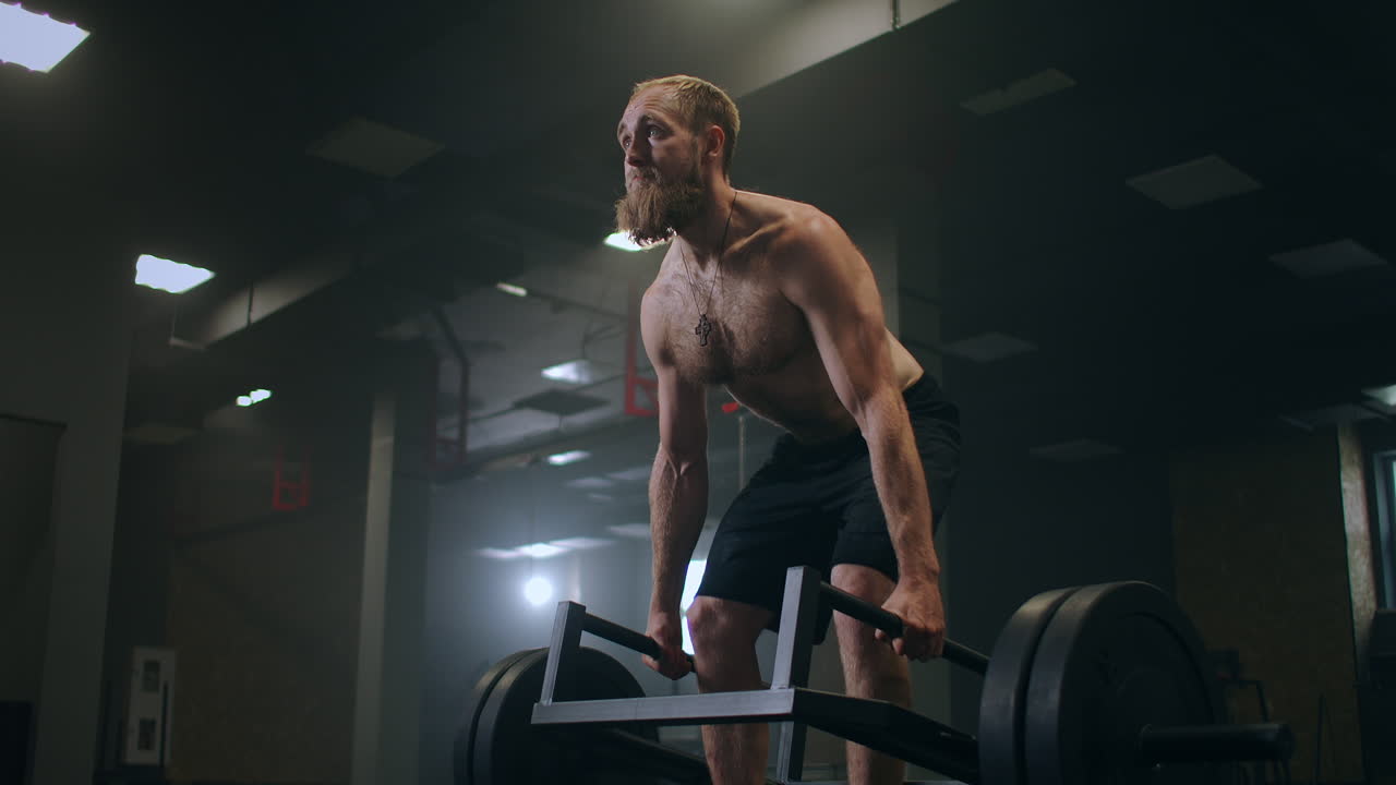 Un uomo che solleva pesi pesanti in palestra. Stacchi rumeni con bilanciere in palestra al rallentatore.