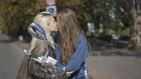 two young women kissing mounted on the motorcycle in the city