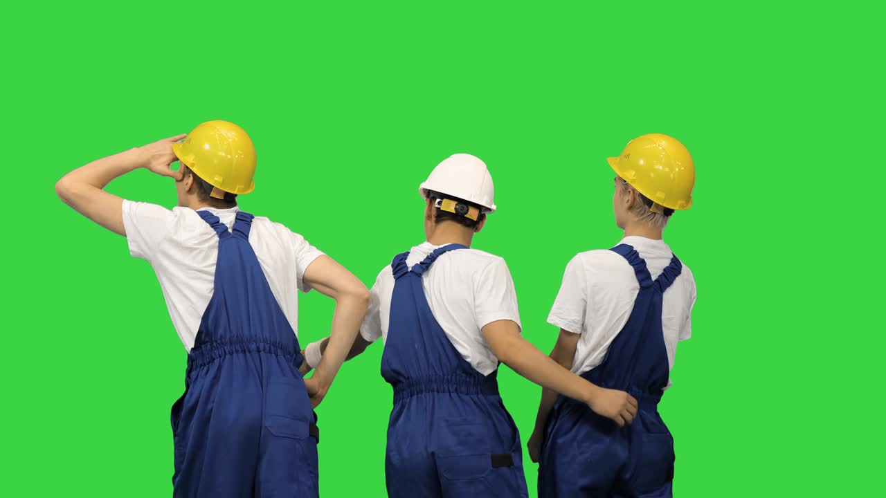 Three male construction workers in hardhats looking at the work site and discussing it with their backs to the camera on a Green Screen, Chroma Key