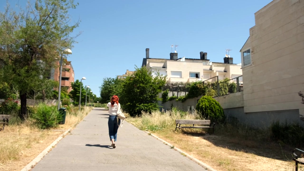 Giovane donna che cammina lungo un sentiero suburbano soleggiato