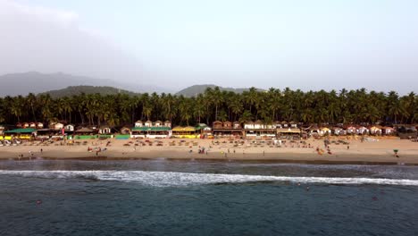 drone flying across the shore of a beach in a tropical sunny beach with tourists, india, goa, palolem