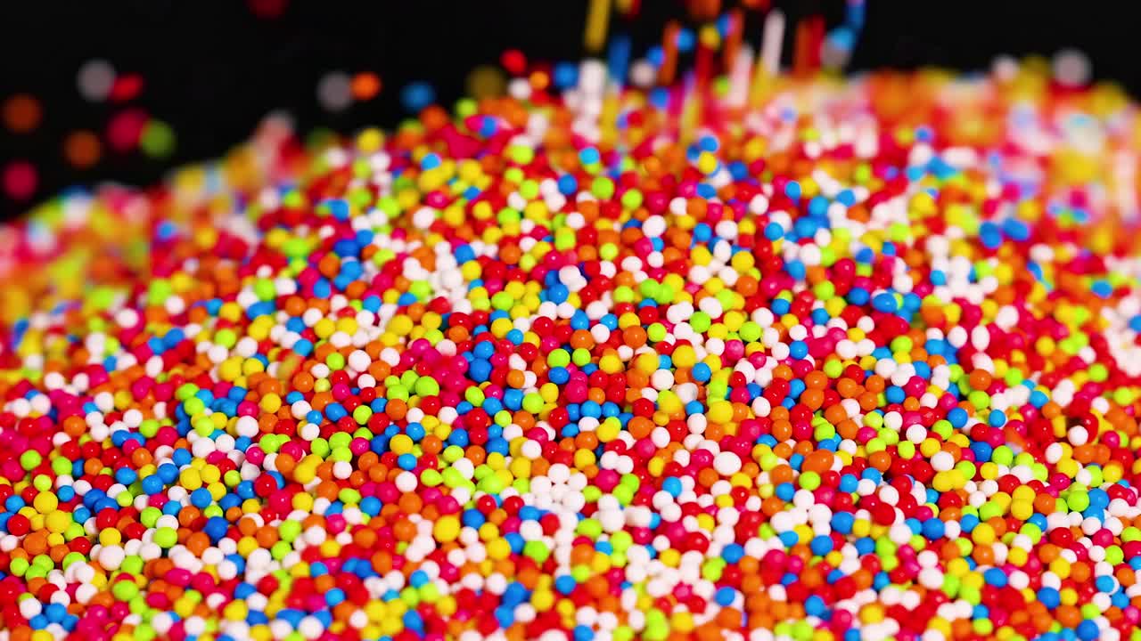 A detailed view of vibrant sprinkles accumulating in a colorful mound against a dark background.