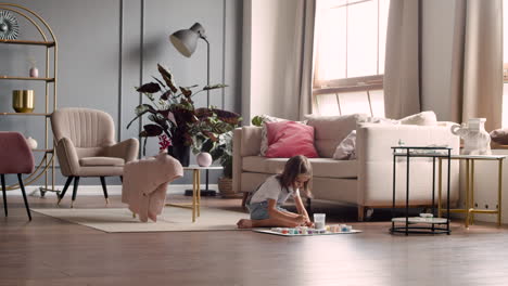 wide view of blonde girl sitting on the floor and painting animal pieces in living room