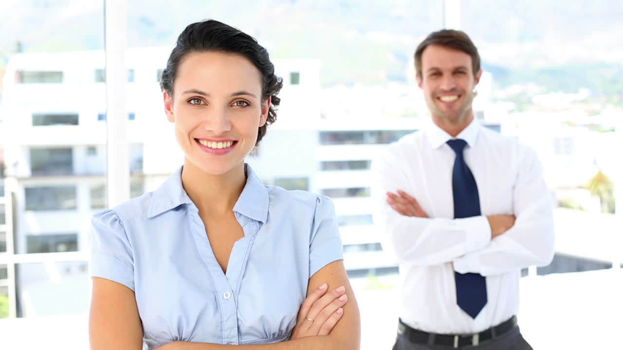 una mujer de negocios bonita sonriendo a la cámara con un colega detrás de ella