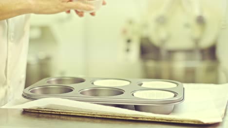 Confectioner-putting-paper-cups-into-baking-forms-for-muffins