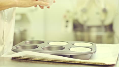 confectioner putting paper cups into baking forms for muffins