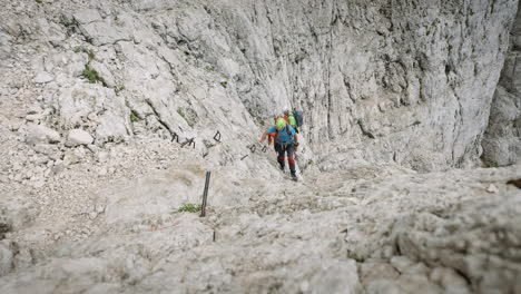 Hikers-climbing-upa-mountain-on-rocks,-camera-moving-away-from-them