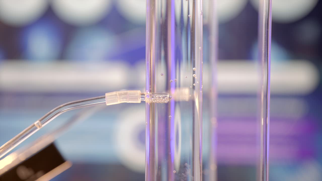Bubbles of hydrogen gas emerge from a small tube into a glass cylinder filled with water