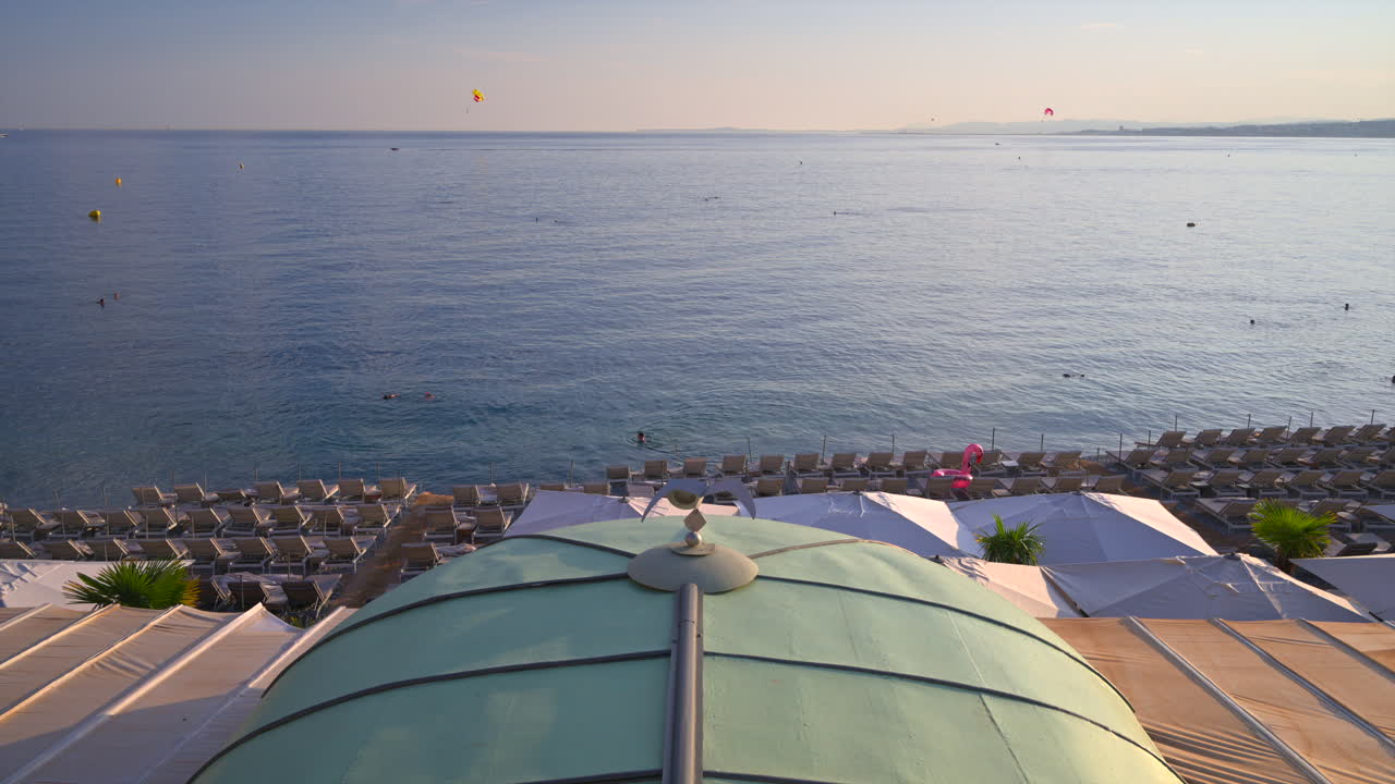 Aerial view of multiple, empty loungers on the beach, with people swimming in the sea at sunset in Cannes, France