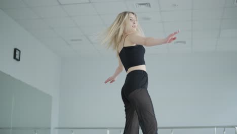 chica en forma con ropa negra actuando contemporáneamente. bailarina muestra movimientos fluidos, cuerpo y manos ondas en la habitación blanca. coreografía de danza de ballet moderno. joven se mueve suavemente