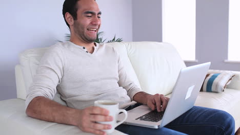 hombre guapo usando su portátil bebiendo café