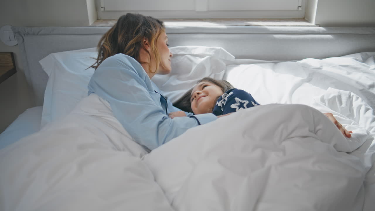 Resting mom child lying cozy white bedroom closeup. Smiling lady stroking girl