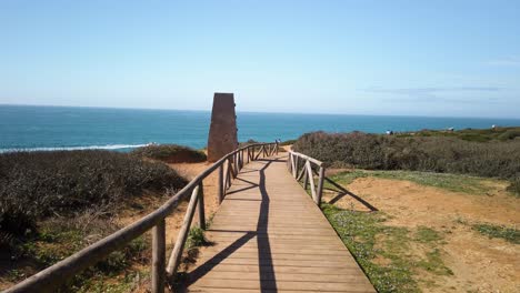 pov walking on wooden beach path toward ocean past grassland