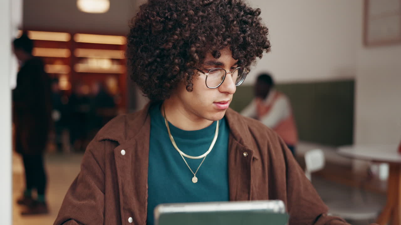 Homem com cabelo cacheado trabalhando em um tablet em um café