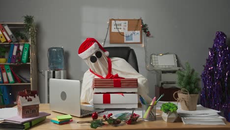 ghost in santa hat with christmas gifts at office desk
