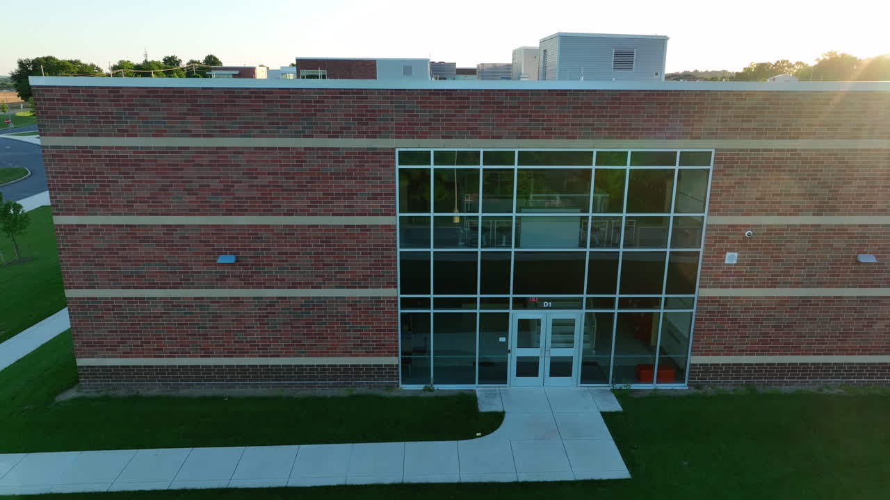 Aerial truck shot of entrance to American elementary school. Brand new school. Spring sunset over the roof of educational building. No people