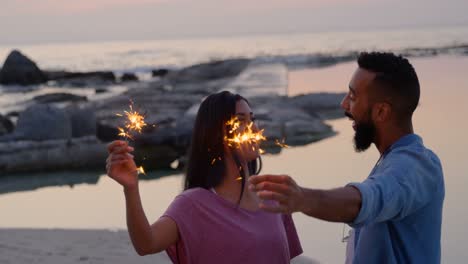 joven pareja feliz de raza mixta divirtiéndose con chispas en la playa 4k
