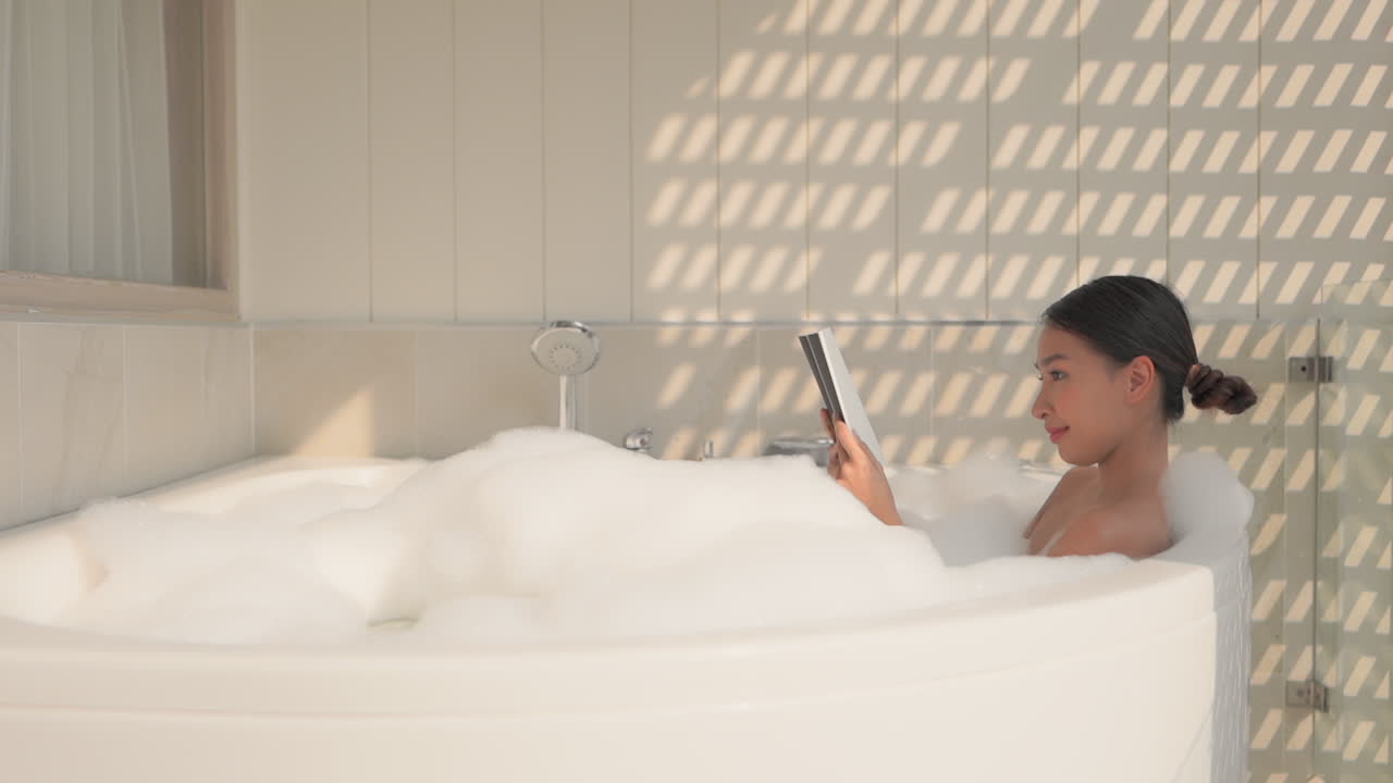 Static shot of attractive young asian woman relaxing, reading in a bubble bath