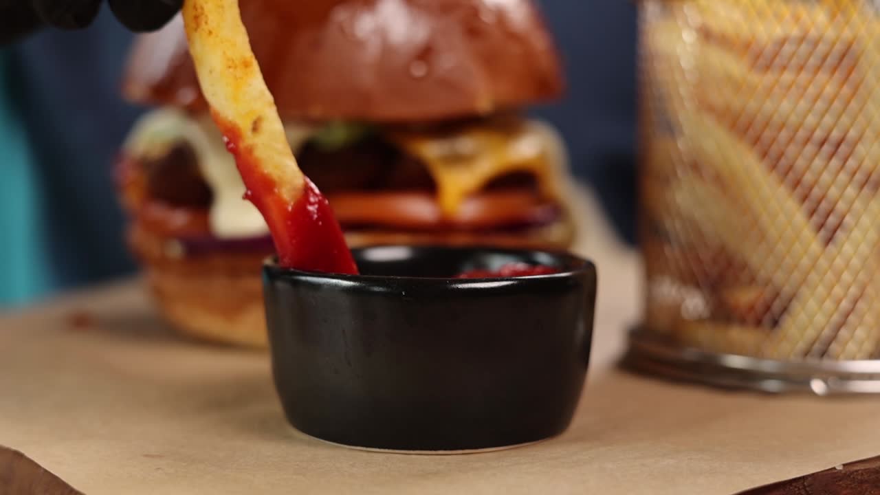 Intingere a mano patatine fritte nel ketchup con hamburger sullo sfondo