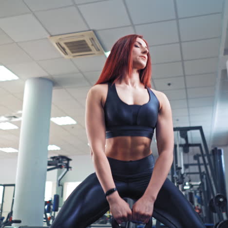 muscular red-haired female with heavy kettlebell. woman with athletic body lifting hard weight to train her muscles in sport center.