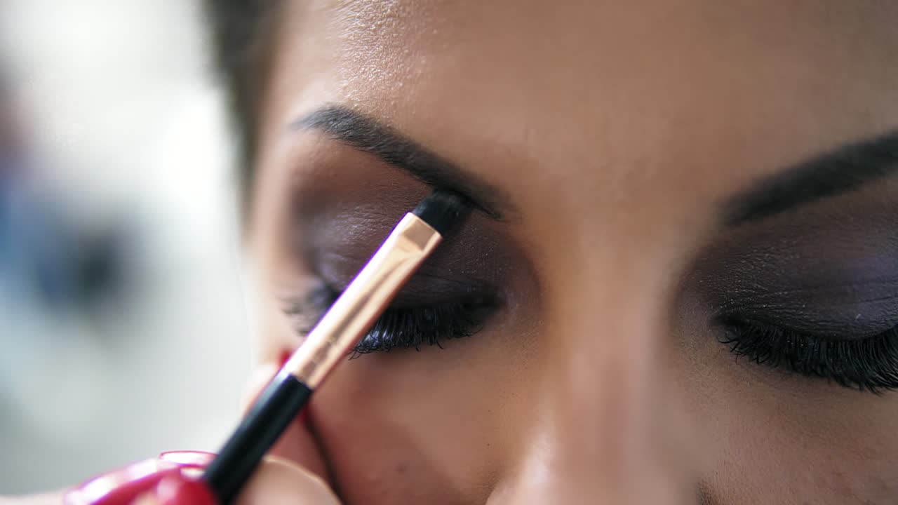vista de cerca de las manos del maquillador usando pincel para pintar cejas para un modelo con pestañas postizas