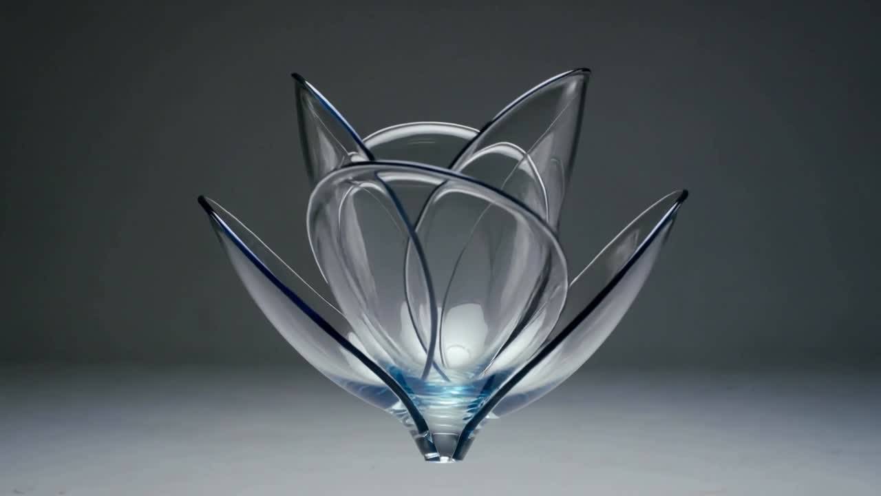 Starting closed, rotating multi-petal glass sculpture opening revealing layers in studio, blue base