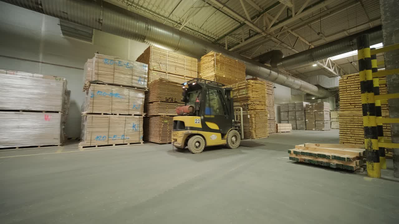 Carretilla elevadora moviendo pilas de madera en un almacén grande