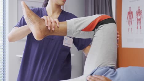 diverse female physiotherapist and senior male patient in hospital physical therapy session on leg