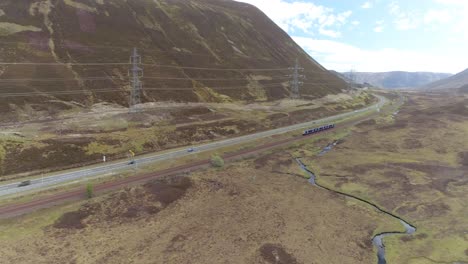 Luftaufnahme-Von-Links-Nach-Rechts-über-Die-Hochlandbahnlinie-Mit-Blick-Nach-Süden,-Wobei-Ein-Nahverkehrszug-Durch-Den-Rahmen-Fährt