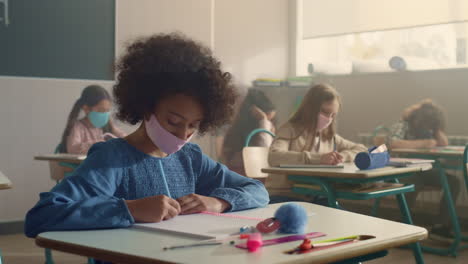 students in medical masks sitting at school desks during coronavirus pandemic