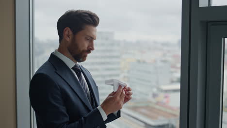 Manager-Mit-Papierflieger-Steht-Am-Fenster-Und-Blickt-Aus-Nächster-Nähe-Auf-Die-Stadtlandschaft.