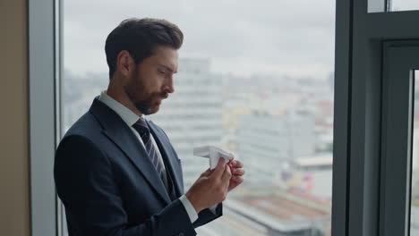 manager holding paper airplane standing at window looking cityscape close up.