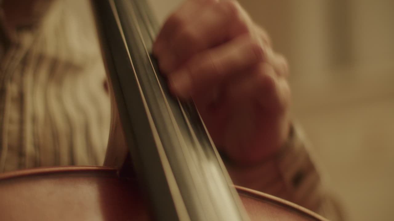 Handheld close up shot of the left hand of a cellist moving over the strings of a cello, doing vibrato with the hands