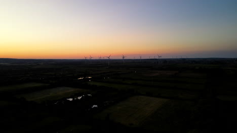 Toma-Aérea:-Movimiento-Panorámico-Lateral-Sobre-El-Parque-Eólico-Puck-Al-Atardecer,-Silueta-De-Turbinas-Eólicas-Giratorias-Sobre-Fondo-De-Cielo-Naranja,-Pomorskie,-Polonia