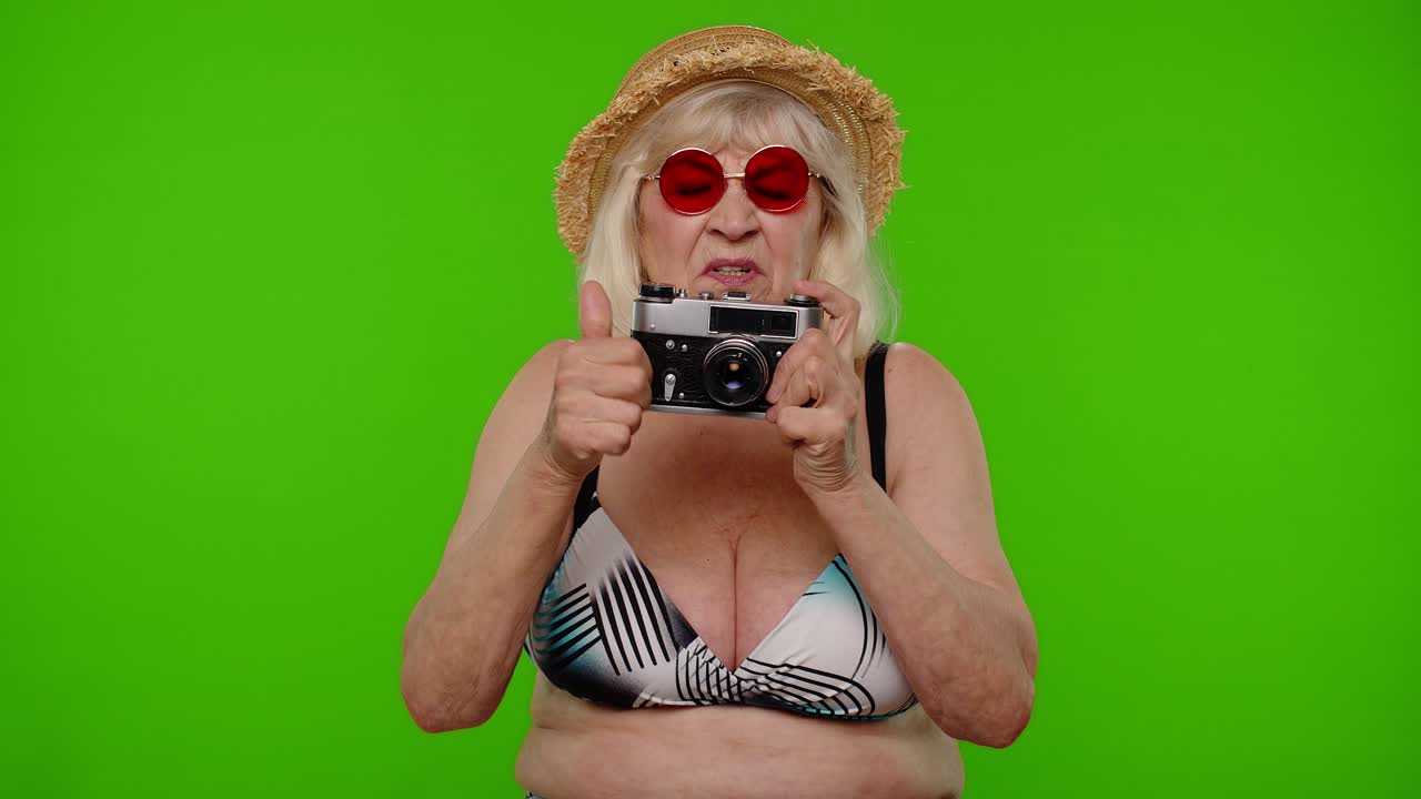 성숙한 여성 사진작가 선글라스를 입은 여행자가 레트로 카메라, 크로마 키로 사진을 찍습니다.