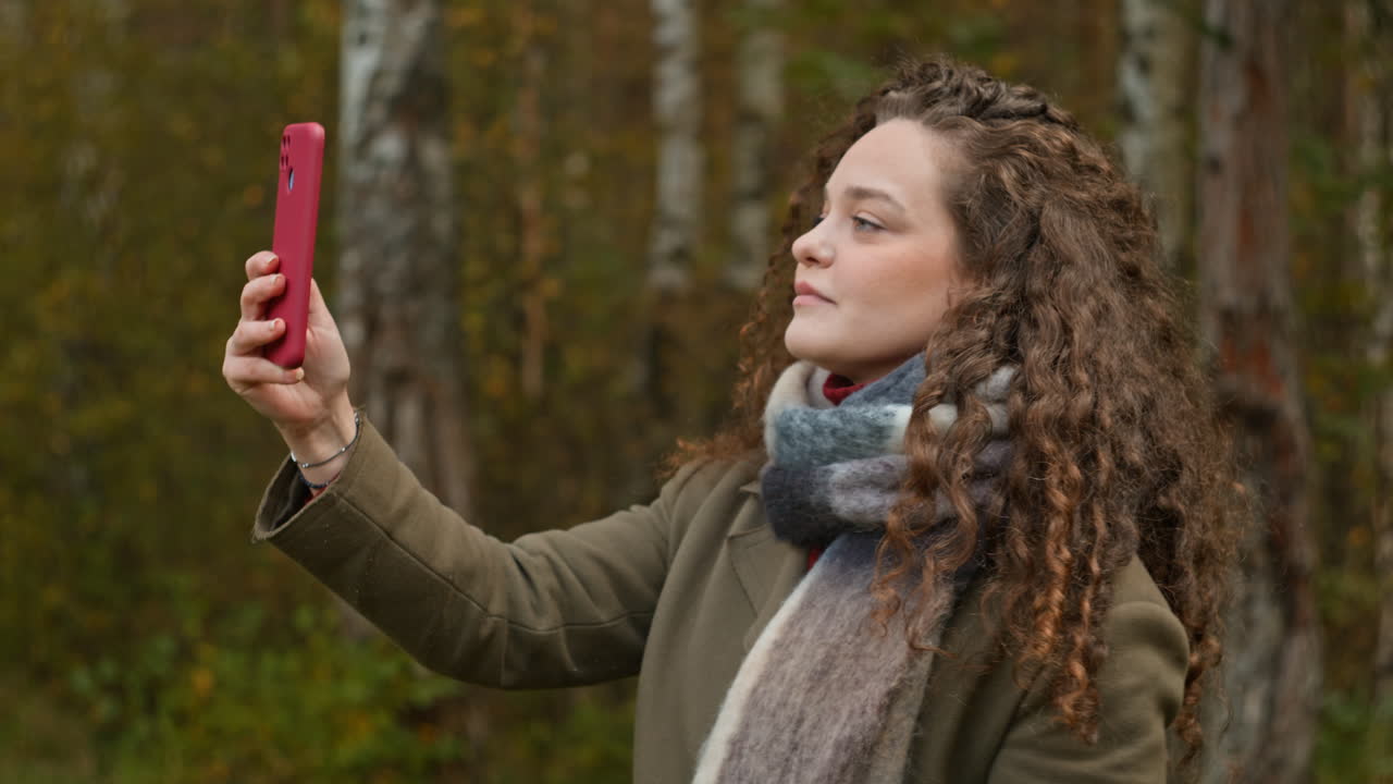 Woman with curly hair taking a photo in the forest